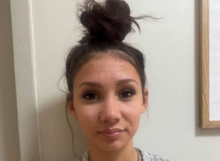 Person with bun hairstyle against white wall.