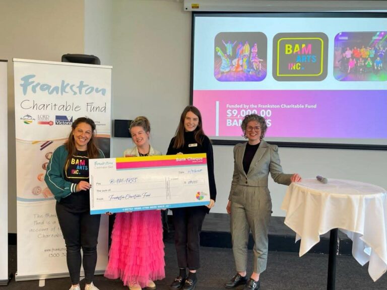 Four people holding large donation cheque indoors.