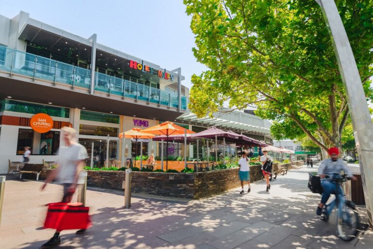 People walking past outdoor cafes on sunny street