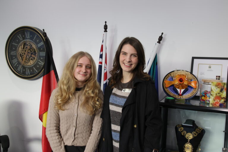 Two women smiling, standing near Australian flags.