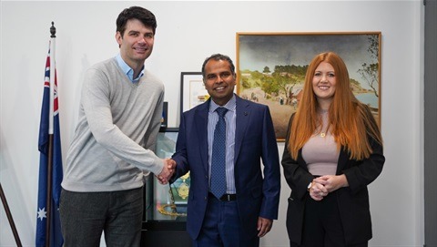 Three people smiling, shaking hands in office.