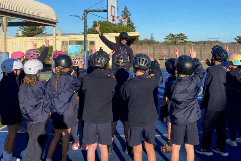 Children with helmets listen to coach outdoors.