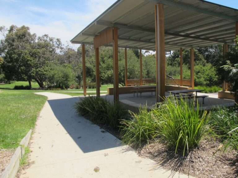 Covered picnic area in sunny parkland landscape.