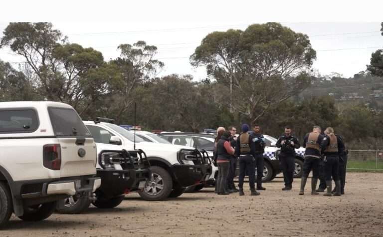 Group near parked police vehicles in rural Australia.