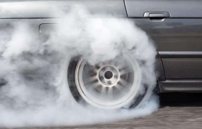 Car tyre spinning, creating smoke on road.