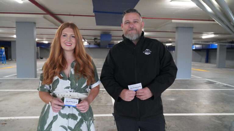 Two people in a parking garage holding cards.