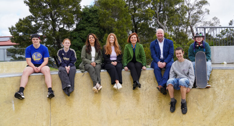 Group sitting on skatepark ledge outdoors.