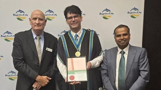 Three men at Frankston City event, one holds award.