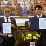 Two men holding certificates in a formal meeting room.