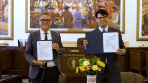 Two men holding certificates in a formal meeting room.