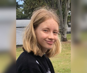 Person smiling outdoors in a park setting.